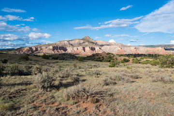 Fototapeta na wymiar Mountain peak, colorful cliffs, and vast desert landscape underneath dramatic blue sky and clouds at Ghost Ranch near Abiquiu, New Mexico