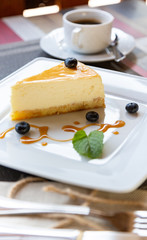 cheesecake with blueberry sauce on white plate and cup of coffee on wooden table