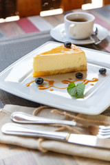 cheesecake with blueberry sauce on white plate and cup of coffee on wooden table