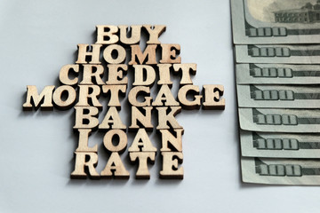 Words BUY, HOME, CREDIT, MORTGAGE, BANK, LOAN, RATE lined with wooden letters about one hundred dollar bills on a white background. Concept of mortgages and buying real estate.