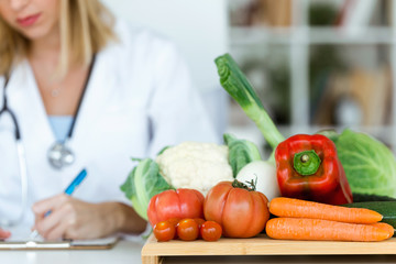 Beautiful young nutritionist working at desk and writing medical records over fresh fruit in the...