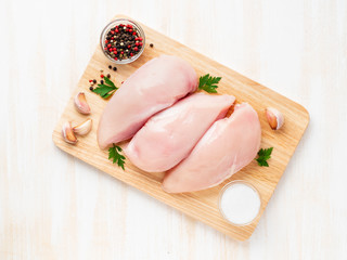 raw chicken breast fillet with spices on a wooden board on white wooden table, top view