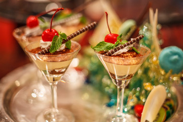 Selective focus of Chocolate creamy trifle in beautiful cocktail glasses with fresh red ripe cherry fruit and chocolate spiral stick topping on table background. Delicious Healthy dessert concept