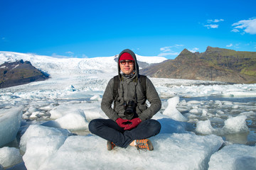 Fototapeta na wymiar A traveler sitting on small ice shelf and doing meditation at Jokulsarlon Glacier Lagoon in Southeast Iceland.