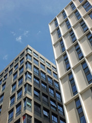 vertical view of a white high white concrete buildings with sunlight and blue sunny sky reflected in the windows