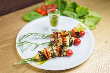 vegetable shish kebab on skewer of rosemary with sauce, on a white plate