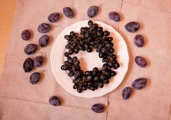 Black grapes on plate and plums near. Top view.