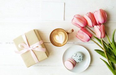 Blueberry and strawberry flavored french macaron desert cakes, brown cappuccino coffee cup, heart shape latte art, craft paper wrapped present tulip flowers. Isolated background, close up copy space