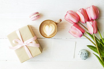 Blueberry and strawberry flavored french macaron desert cakes, brown cappuccino coffee cup, heart shape latte art, craft paper wrapped present tulip flowers. Isolated background, close up copy space