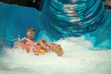 European boy gliding down slide in aqua park. - 220147615