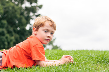 A young boy looking at the camera while laying on some grass