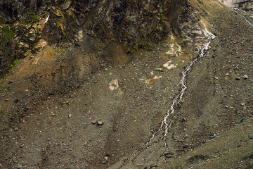 Detailed natural texture of slope from loose stones. Mountain water stream flows down mountainside. Small waterfall on rock. Unusual landscape of majestic nature.
