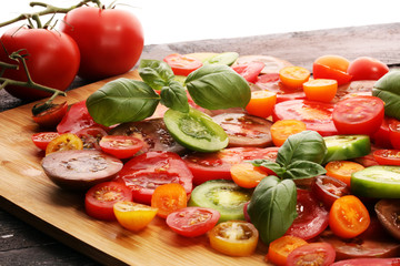 various colorful tomatoes and basil leaves on rustic table.