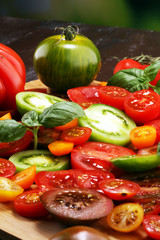 various colorful tomatoes and basil leaves on rustic table.