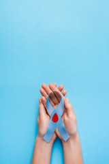 the blue ribbon awareness with red blood drop in woman hands isolated on a blue background. World...