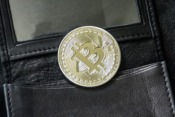 Bitcoin metal coin laying on black leather wallet