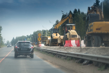 a black suv car on the road with concrete white and red blocks from one side and safety rail or barrier from other side. Part of the highway is under construction