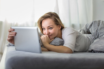 Pretty, young woman in her bed using her tablet computer, staying up to date with news and socail networks she likes(color toned image; shallow DOF)