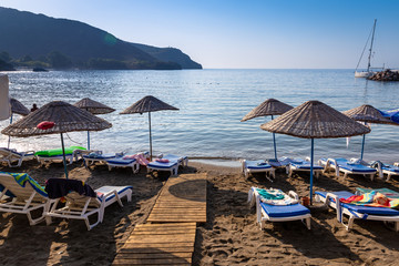 An empty beach in a heavenly bay. Beach umbrellas with sunbeds and towels on towels. Sea and sky...