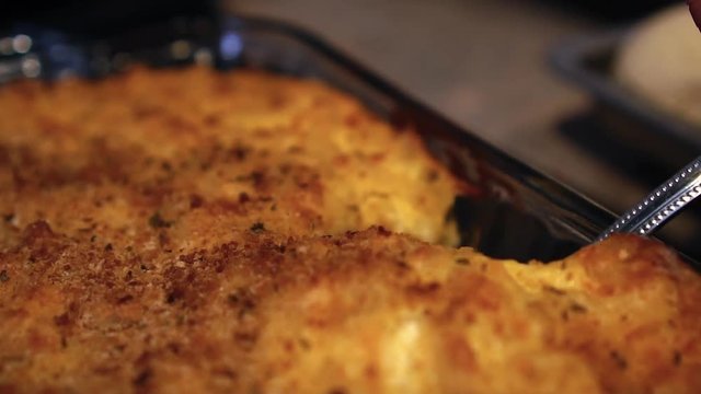 Spoon scooping up a helping of baked macaroni and cheese, in slow motion