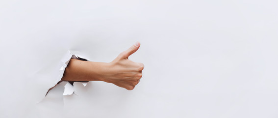 Thumbs up sign. The hand came out through the hole in white paper and shows finger up. Like, cool,...