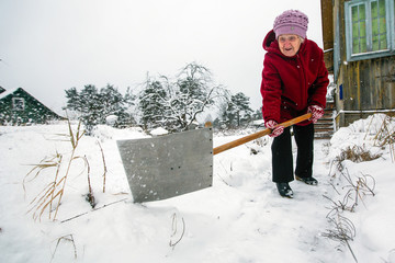 Elderly woman cleans snow near the his rural house at vinter.