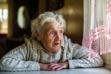 Gray-haired elderly woman sits and looks out the window.