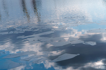 Clouds reflected in the water. Pieces of ice on the water in early spring.