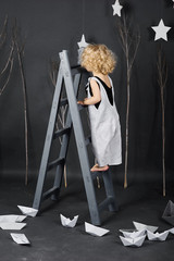 a little beautiful curly girl near the ladder on a grey background
