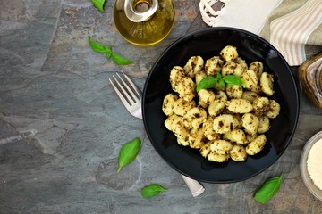 Gnocchi with pesto sauce. Top view scene over a dark stone background with copy space.