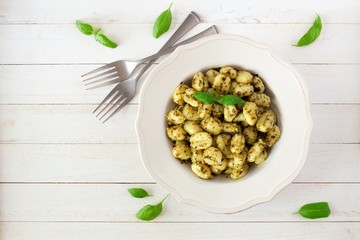 Plate of gnocchi with pesto sauce. Top view over a white wood background.