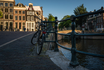 Fototapeta premium A lonely bicycle tied to a canal fence in the city of Amsterdam at sunset, the Netherlands
