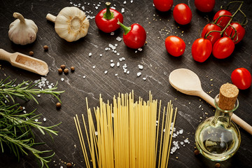 cooking ingredients for cooking composed of tomatoes, garlic, salt, olive peppers and pasta on a black table