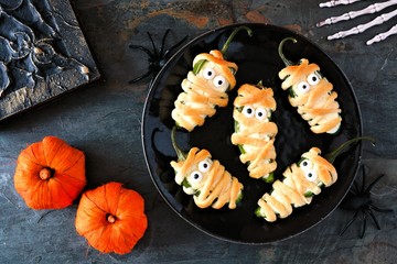 Halloween mummy jalapeno poppers, top view with decor on a dark stone background