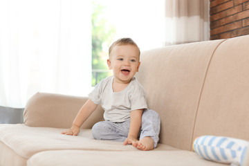 Adorable little baby sitting on sofa at home