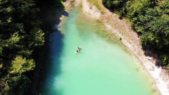 vue a&eacute;rienne sur un lac vert &eacute;meraude entour&eacute; de for&ecirc;t avec une personne qui pagaye sur une planche