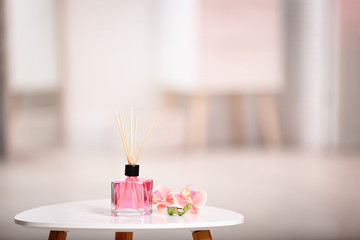 Aromatic reed air freshener and flowers on table against blurred background