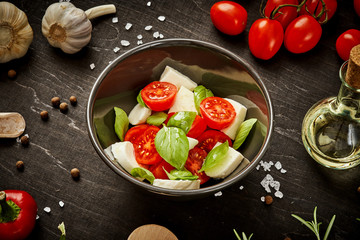delicious salad with cherry tomatoes mozzarella and basil in a bowl on a black wooden table