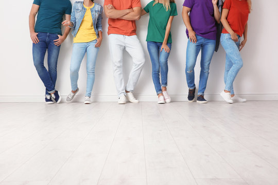 Group of young people in jeans and colorful t-shirts near light wall