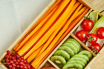 box with delicious carrots, apple, kiwi, cherry tomatoes and redcurrant on a wooden table
