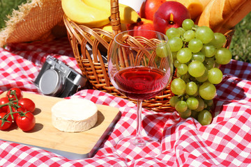 Basket with food and glass of wine on blanket prepared for picnic in park