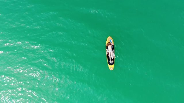 vue a&eacute;rienne sur une jeune fille qui se repose &eacute;tendue sur son paddle en plein milieu d'un lac aux eaux vertes