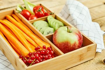 box with delicious carrots, apple, kiwi, cherry tomatoes and redcurrant on a wooden table