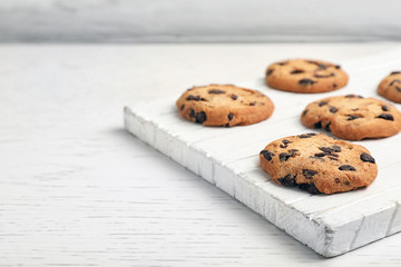 Wooden board with tasty chocolate cookies on light table