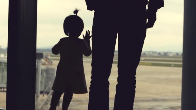 Father and daughter looking out the window with view on airport area. Planes can be seen in the distance.