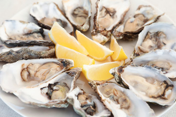 Fresh oysters with cut juicy lemon on plate, closeup