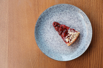 Plate with slice of cherry cake on wooden table, top view
