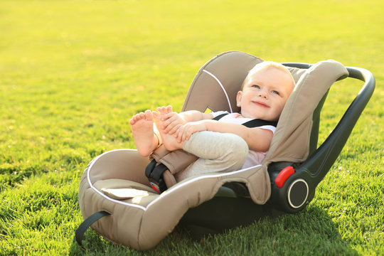 Adorable baby in child safety seat on green grass