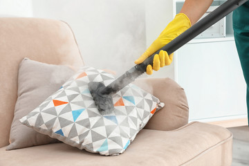 Janitor removing dirt from sofa cushion with steam cleaner, closeup