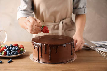 Baker decorating fresh delicious homemade chocolate cake with berries on table, closeup
